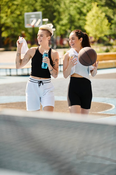 Kaksi urheilullista nuorta naista seisoo rinta rinnan pitäen koripalloa ulkona, huokuen itseluottamusta ja ystävyyttä.. - Valokuva, kuva