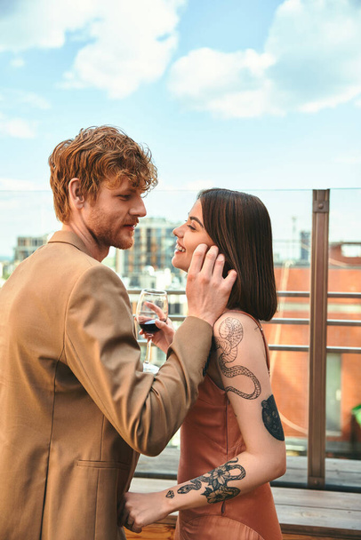 Muž a žena stojí bok po boku a žena drží sklenici vína. Zdá se, že sdílejí okamžik intimity a spojení. - Fotografie, Obrázek
