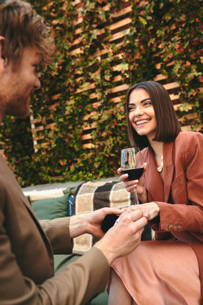 Een man in een pak met een glas wijn naast een vrouw in een cocktailjurk, die een moment van verbondenheid en intimiteit deelt - Foto, afbeelding