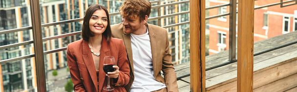 Um homem está graciosamente ao lado de uma mulher que segura um copo de vinho, exalando sofisticação e charme - Foto, Imagem