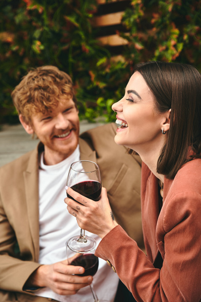 Mężczyzna i kobieta siedzą obok siebie, brzęcząc kieliszkami wina w romantycznym geście. - Zdjęcie, obraz