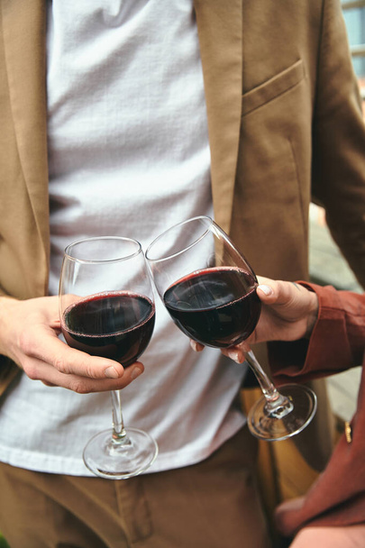 Ένας κομψός άντρας με ένα ποτήρι σε κάθε χέρι γεμάτο με κόκκινο κρασί, επιδεικνύοντας κομψότητα και φινέτσα - Φωτογραφία, εικόνα