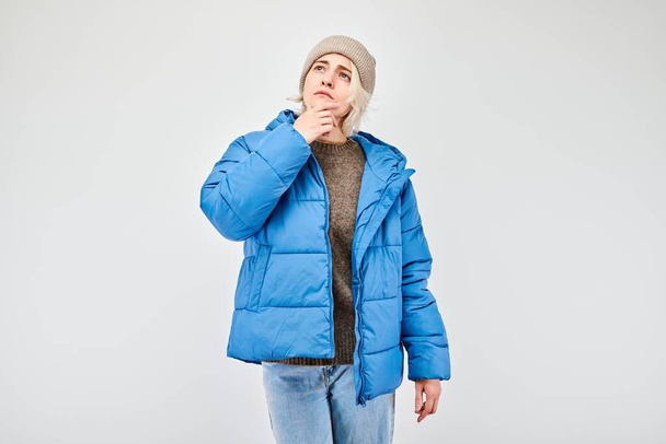 Woman in winter attire with pensive expression, thinks, chooses isolated on light background - Foto, Imagem