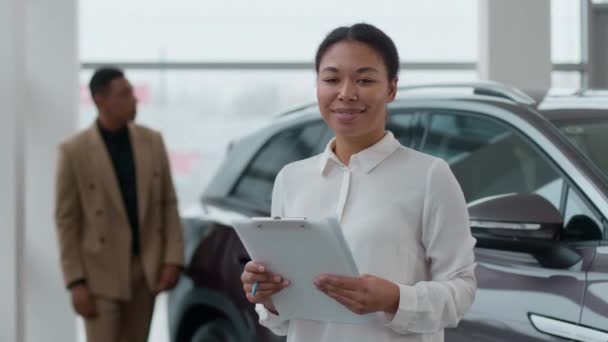 Retrato de la mujer afroamericana vendedor de coches sonriendo posando en el centro de concesionarios de automóviles vendedor gerente femenino distribuidor con portapapeles ayudar al cliente a comprar un nuevo servicio profesional de automóviles - Imágenes, Vídeo