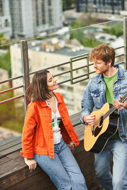 Мужчина и женщина страстно играют на гитаре на балконе, создавая вместе прекрасную музыку под открытым небом - Фото, изображение