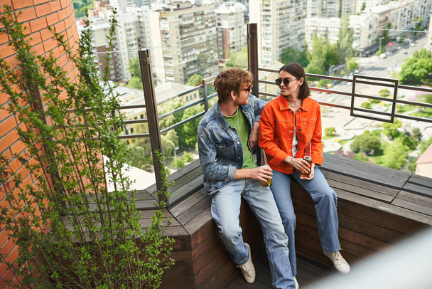 A couple seated together on a rooftop, enjoying the view and each others company against the backdrop of the city skyline - Photo, Image
