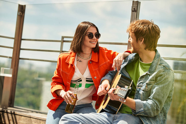 Een man zit naast een vrouw, die een gitaar vasthoudt. Ze verschijnen betrokken in een muzikaal gesprek, ondergedompeld in het creëren van melodieën samen - Foto, afbeelding