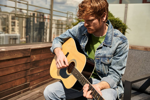 Un uomo di talento siede su una panchina, con passione a suonare la chitarra, perso nella musica sotto il cielo aperto - Foto, immagini