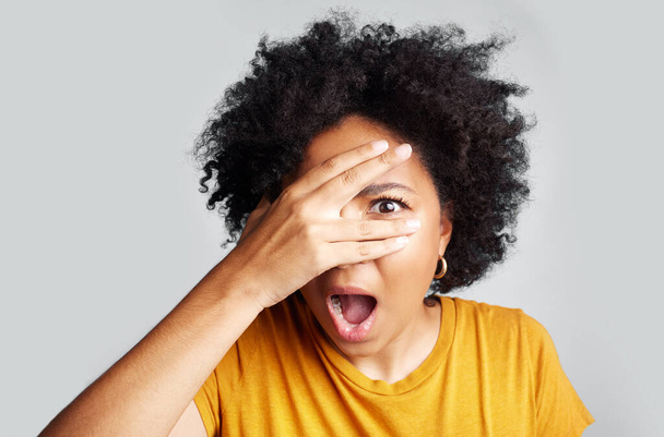 Surprise, wow and woman peeking through hand isolated on a white background in studio. Shocked, face and African female person shy, embarrassed or fear, scared or shame, emoji or mind blown portrait - Photo, Image