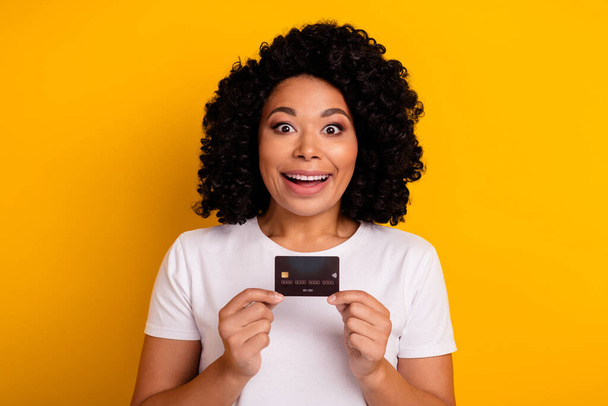 Photo of overjoyed ecstatic impressed woman with chevelure presenting credit card astonished staring isolated on yellow color background. - Foto, imagen