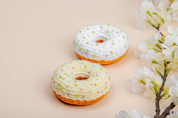 Handgemaakte gehaakte donuts met bloeiende kersentakken. Feestelijke Pasen, wenskaart, creatief ambachtelijk concept. Trendy abrikozenachtergrond, platte lay, kopieerruimte - Foto, afbeelding