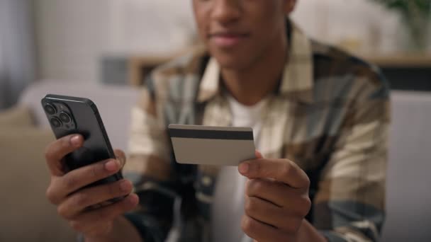 Nerozpoznatelný Afroameričan držet plastové kreditní karty smartphone virtuální peníze bezhotovostní finanční transakce platit on-line internetové platby bankovnictví mobilní telefon nakupování chlap domácí koupit - Záběry, video