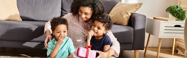 feliz hermosa mujer afroamericana posando con sus dos hijos pequeños con presente, Día de las Madres - Foto, Imagen