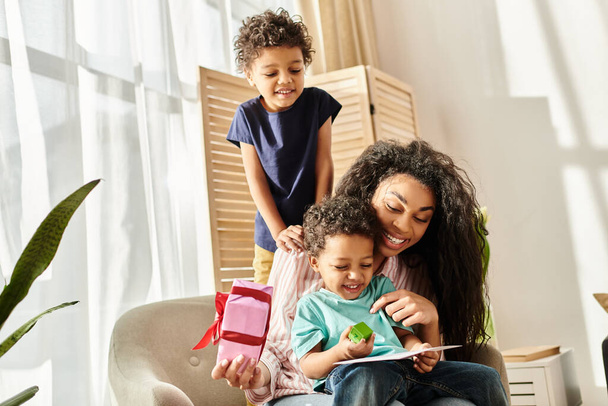 fröhliche afrikanisch-amerikanische Frau mit ihren süßen Söhnen, Geschenk und Postkarte, Muttertag - Foto, Bild