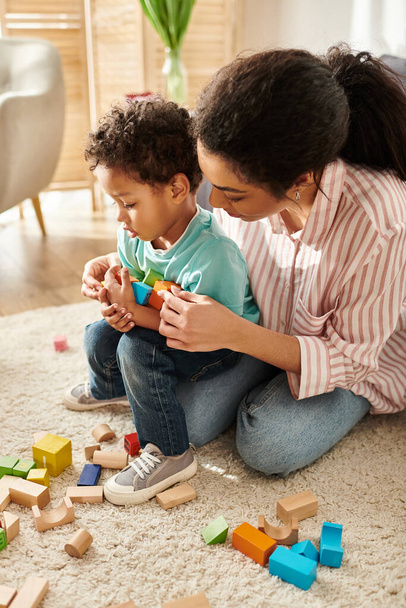 boa aparência afro-americana mãe jogando ativamente com seu pequeno filho bonito, enquanto na sala de estar - Foto, Imagem