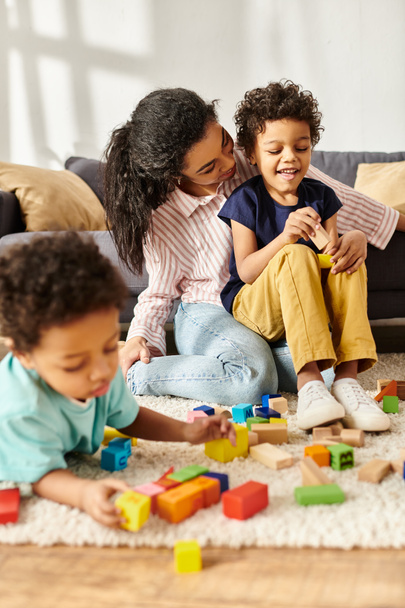 focus op vrolijke Afrikaanse Amerikaanse moeder en haar zoon naast haar andere wazig zoon spelen met speelgoed - Foto, afbeelding