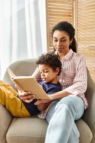 joyful beautiful african american mother reading interesting book with her adorable jolly son - Photo, Image