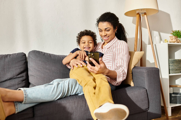 cheerful african american mother hugging her little son and looking at smartphone together with him - 写真・画像