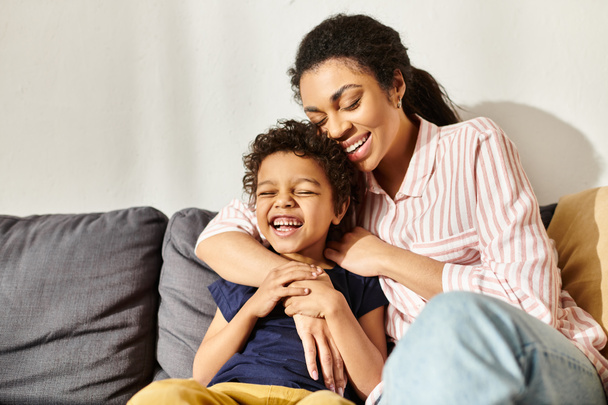 Neşeli, sevecen, Afro-Amerikan annesi oturma odasında gülümseyen oğluna sarılıyor. - Fotoğraf, Görsel