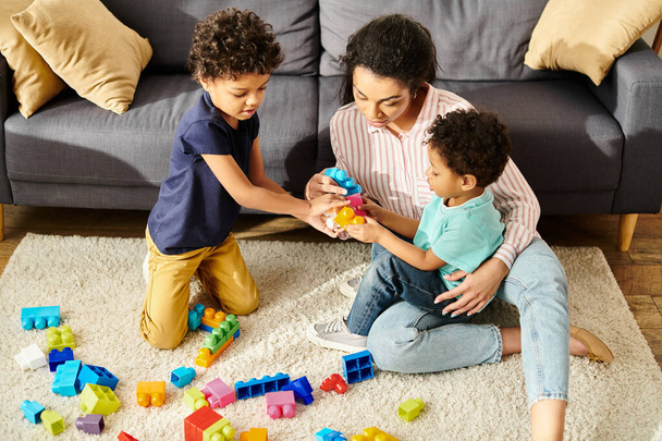 piękne Afryki amerykański matka w przytulny strój bawiąc się z jej słodkie małe synowie w salonie - Zdjęcie, obraz