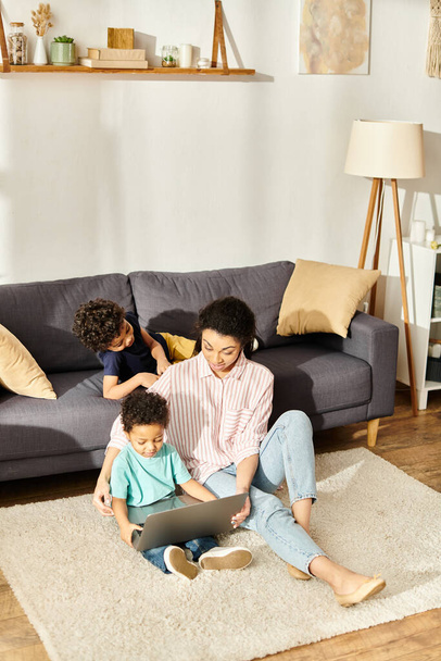 vrolijk afrikaans amerikaans moeder het hebben van plezier met haar kleine zonen in voor laptop thuis - Foto, afbeelding