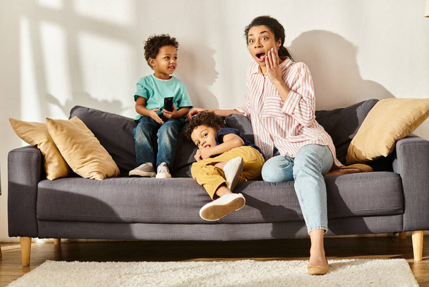 zaskoczony piękne afrykańskie amerykańskie kobieta w homewear oglądać filmy z jej urocze synów - Zdjęcie, obraz