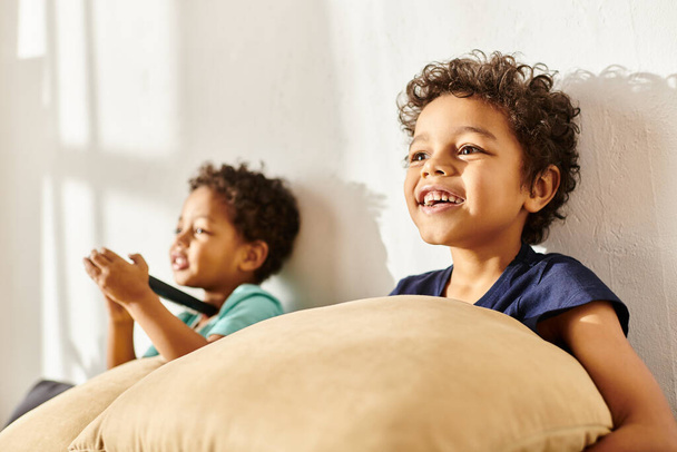 Yastık tutan neşeli Afro-Amerikalı çocuğa odaklan ve bulanık tatlı kardeşinin yanında televizyon izle. - Fotoğraf, Görsel
