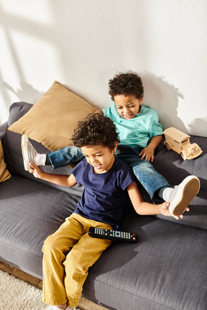 joyful adorable brothers in homewear having fun while sitting in front of TV in living room - Photo, Image