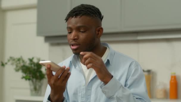 Afrikkalainen amerikkalainen mies vakava biracial mies pidä älypuhelin kaiuttimen puhuminen puhua puhua matkapuhelin kaiutin mukavuutta käyttö laskenta sormilla kaveri tallentaa ääniviestin vastaajaan keittiössä - Materiaali, video
