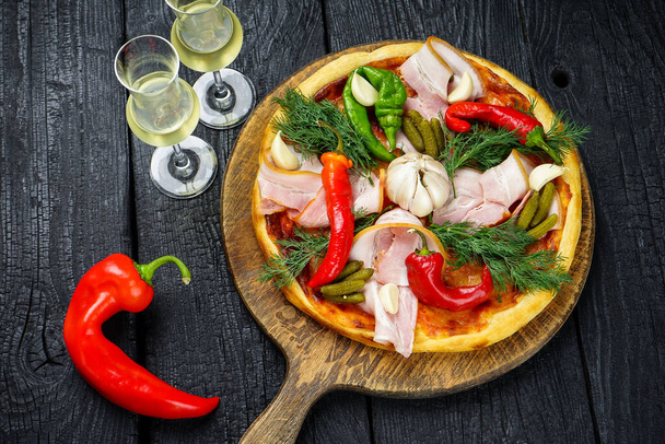 pizza met ham, komkommers, knoflook, rode paprika 's en kaas op een houten tafel. - Foto, afbeelding