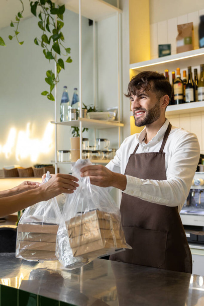 Bearded man bartender handing pizza boxes for unrecognizable client in pizzeria - Fotó, kép