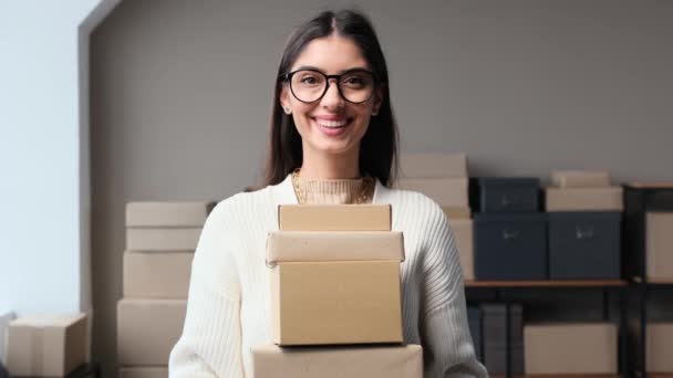 Retrato de una amigable vendedora de tienda online caucásica con cajas de cartón o paquetes con pedidos en almacén u oficina postal. - Metraje, vídeo