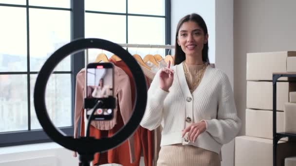 Happy female Caucasian blogger recording video or conducting broadcast with review of clothes for selling in her online shop. E-commerce startup concept. - Footage, Video