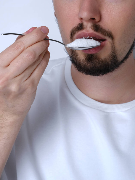 Portret młodego mężczyzny jedzącego cukier łyżeczką z bliska - Zdjęcie, obraz