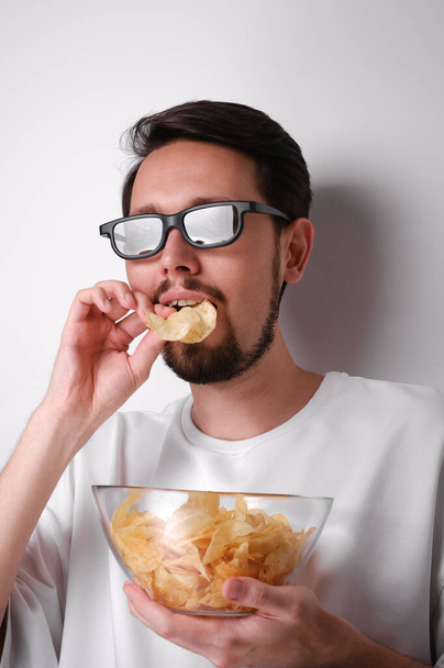 portret młodego mężczyzny oglądającego film w okularach 3D i jedzącego chipsy - Zdjęcie, obraz
