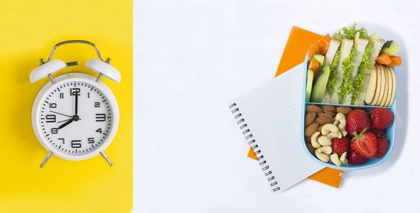 School lunchbox and white alarm clock on the yellow and white background. Top view. Copy space. - Photo, Image