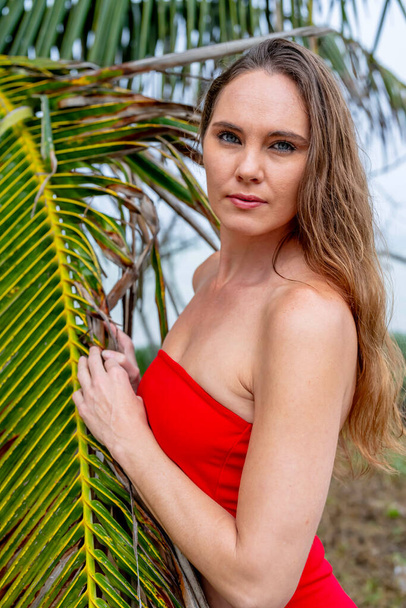 Lenyűgöző barna, ragyogó, élénk piros ruhában, eleganciával díszíti a Karib-tenger partjait, megtestesítő szépséggel a trópusi paradicsomban. - Fotó, kép