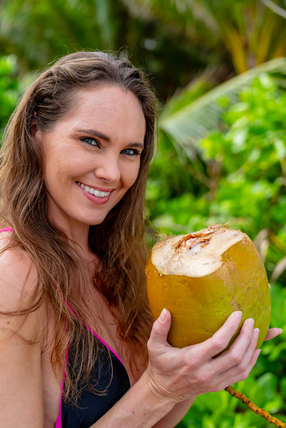 Aurinko-suuteli brunette, koristeltu bikinit, juhlii Karibian autuus hiekkarannalla, jossa yhdistyvät kauneus seikkailu etsiessään kookospähkinöitä - Valokuva, kuva