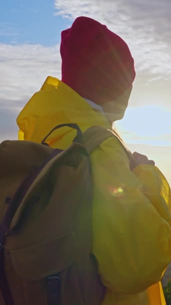 Cámara de cámara lenta sigue a mujer excursionista en impermeable amarillo con mochila. Atractiva chica joven feliz con mochila de senderismo. Puesta de sol en el horizonte en las montañas de la isla de Madeira. - Metraje, vídeo