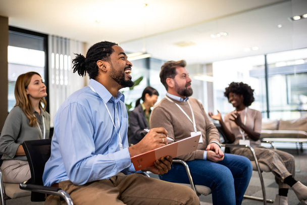 Νεαρός Αφρο-Αμερικανός επιχειρηματίας ακούγοντας μια διάλεξη δασκάλων που είναι στην εταιρεία του. - Φωτογραφία, εικόνα