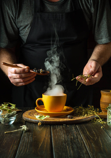 A man prepares tea from the medicinal plants rosehip and chamomile on the kitchen table. Traditional medicine concept at home. - Photo, Image