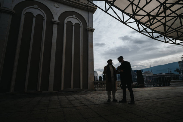 Two men engaged in a serious conversation outdoors by architectural columns. - Photo, Image