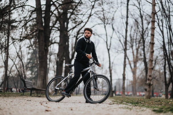 Un uomo d'affari in abbigliamento casual si prende una pausa per pedalare nel parco, riflettendo un equilibrio tra imprenditorialità e salute.. - Foto, immagini