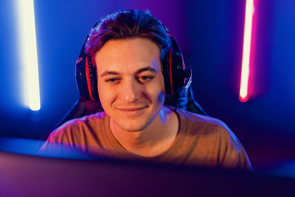 Host κανάλι του gaming smart streamer παίζοντας online παιχνίδι για να είναι νικητής, φορώντας ακουστικά με τους θεατές ζουν ατμό στα μέσα κοινωνικής σε απευθείας σύνδεση για επιλεγμένο ομαδικό διαγωνισμό σε neon light room. Επιδοτούμενο. - Φωτογραφία, εικόνα