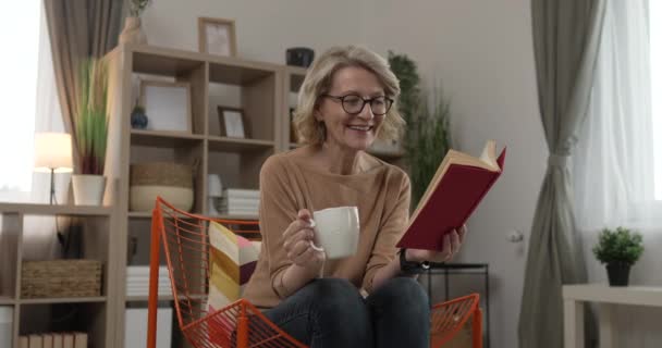 Yetişkin bir beyaz kadın evde kitap okuyor ve gözlük takıyor. - Video, Çekim