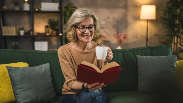 Одна жінка зріла біла жінка читає книгу вдома в окулярах - Фото, зображення