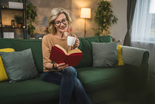 Eine reife kaukasische Frau liest zu Hause Buch und trägt eine Brille - Foto, Bild