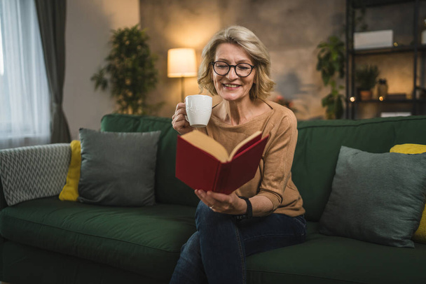 Yksi nainen kypsä valkoihoinen nainen lukea kirjaa kotona kulumista silmälasit - Valokuva, kuva