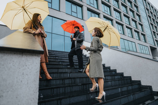 Tre professionisti che trasportano ombrelli colorati che navigano a passi bagnati in città, mostrando una scena della vita urbana quotidiana e pendolarismo con tempo inclemente. - Foto, immagini