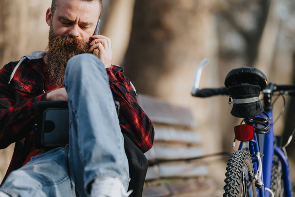 Homem de negócios focado em traje casual trabalhando remotamente em um tablet enquanto sentado ao lado de sua bicicleta em uma área urbana da cidade. - Foto, Imagem